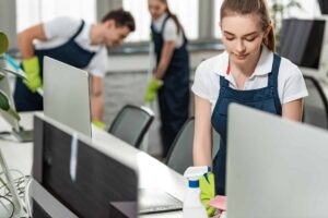 Focused cleaner diligently wipes a desk while colleagues clean the floor in the office. Experience our team's dedication to maintaining a pristine workspace with professional cleaning services.